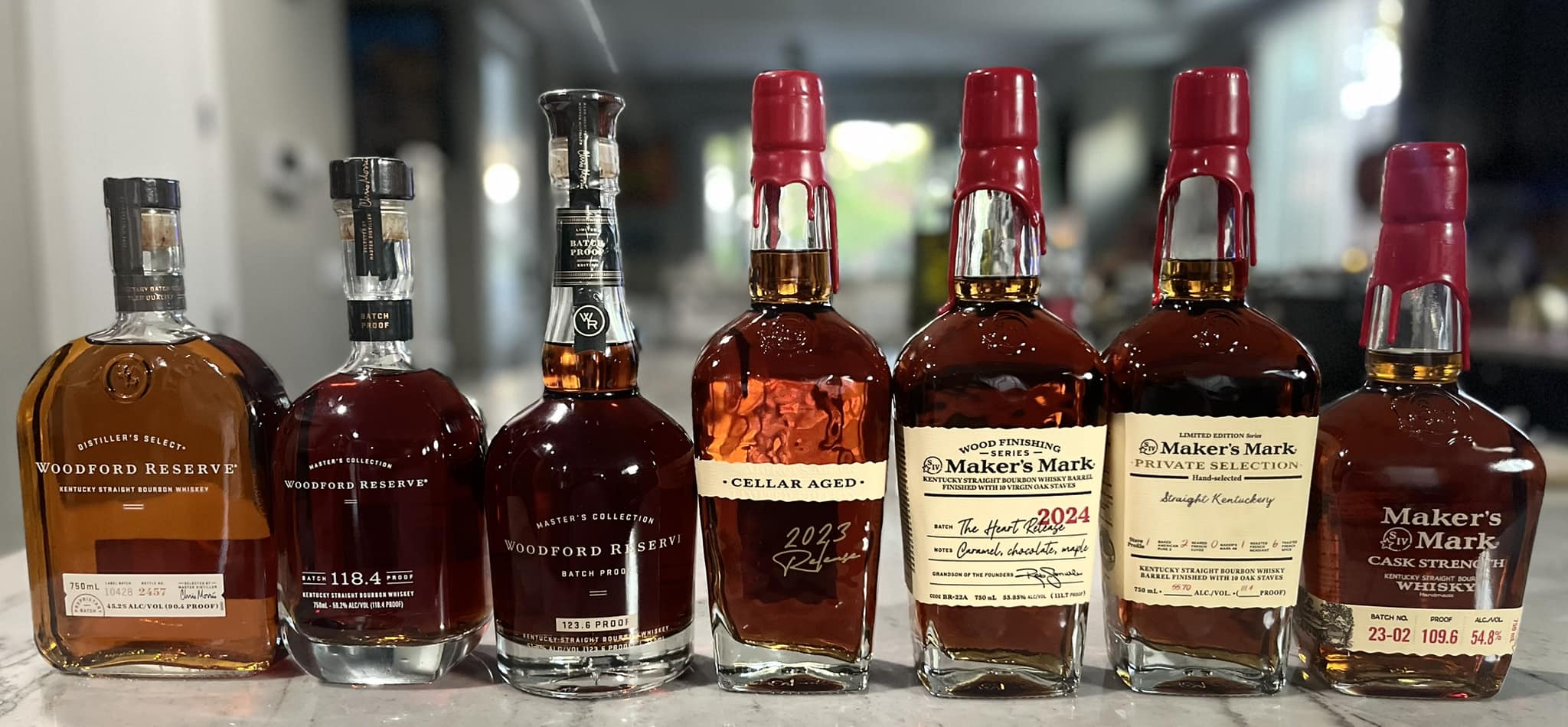 Seven bottles of bourbon lined up left to right on a countertop.