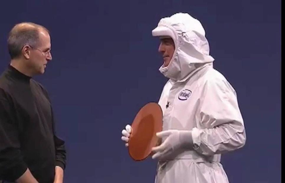 Steve Jobs, left, wearing his traditional black mock turtleneck, looking at Paul Otellini, dressed in a white Intel cleanroom suit (aka “bunny suit”).